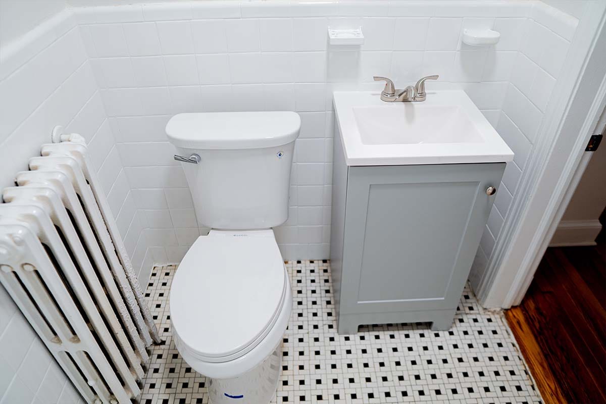 Closeup on new toilet, gray cabinet and sink installed inside an apartment bathroom by JVV Remodeling