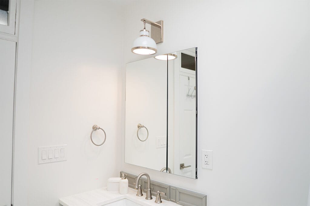 Wide view of new mirror and lighting fixture installed in a hallway bathroom in Takoma DC